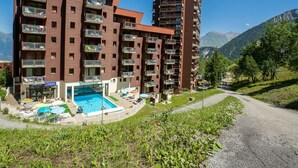 A multi-story hotel with balconies, a swimming pool, and a view of mountains. - Nice apartment for 6 guests with WIFI, pool, TV and balcony (Le Corbier)