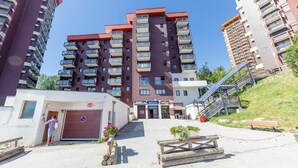 A multi-story residential building with balconies, a small entrance area with a sign, and a staircase leading to an upper level. - Nice apartment for 6 guests with WIFI, pool, TV and balcony (Le Corbier)