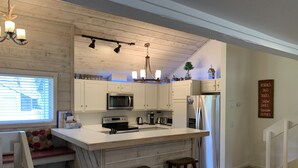 Una cocina moderna con armarios blancos, una isla central, taburetes de bar, horno integrado, microondas y refrigerador.