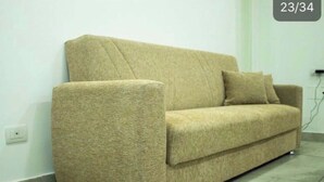 A beige sofa with a cushion against a white wall. - Graphite House 2.0 (Napoli)