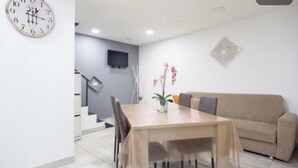 A dining area with a wooden table and chairs, a beige sofa, a wall-mounted clock, and a decorative wall piece. - Graphite House 2.0 (Napoli)