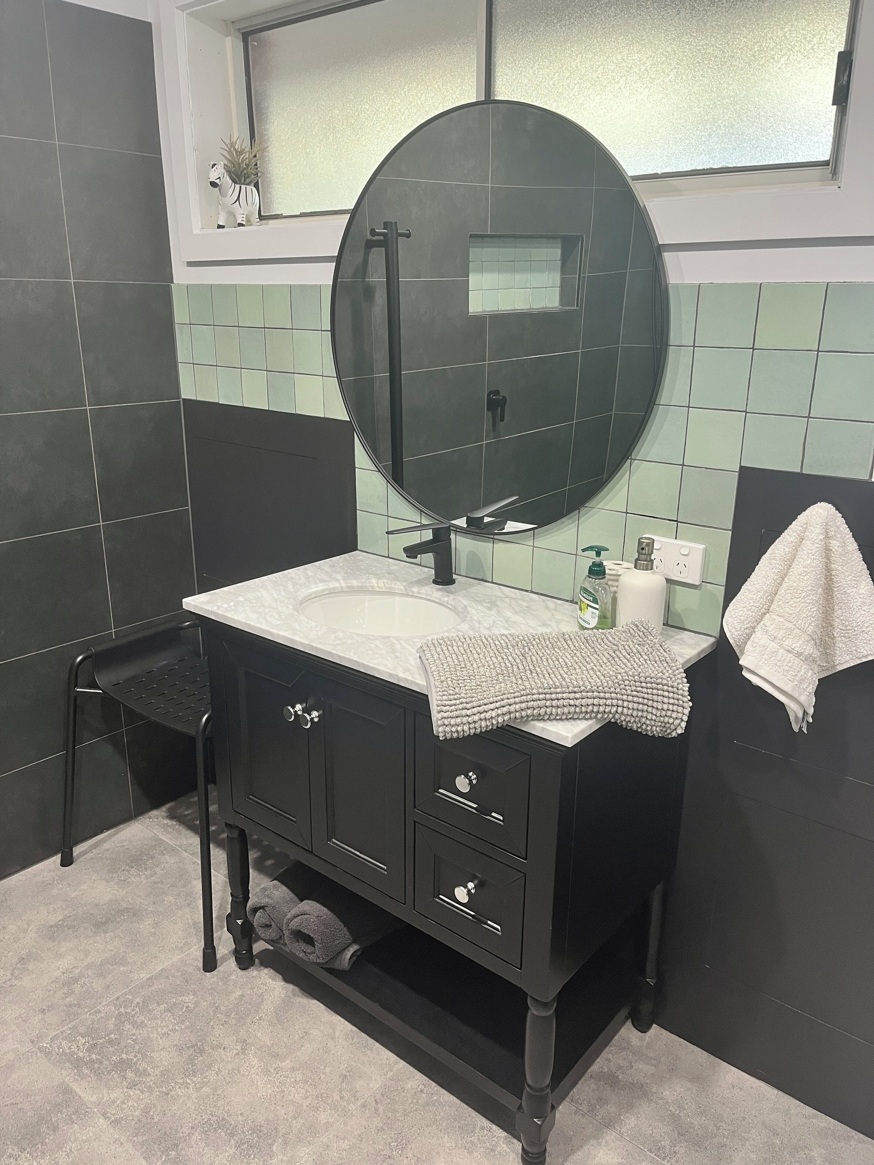 A bathroom with a round mirror, black vanity, and a small window.
