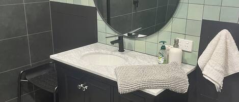 A bathroom with a round mirror, black vanity, and a small window.