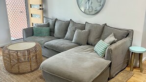 En moderne stue med en modulsofa, et rundt ur, en vævet skammel og et lille sofabord.
