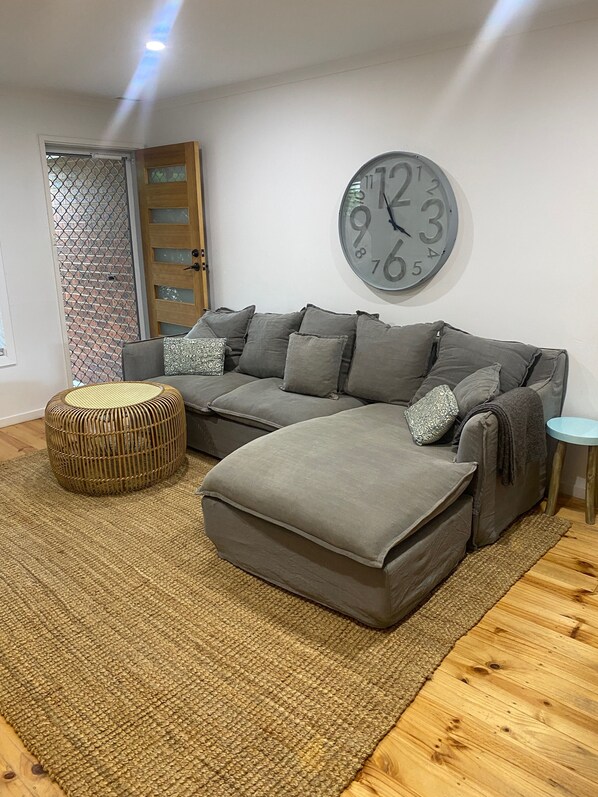 A modern living room with a sectional sofa, a round clock, and a wicker ottoman.