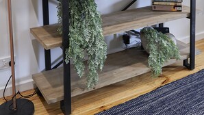 En moderne stue med et fladskærms-tv på væggen, et træsofabord med dekorative planter og en gulvlampe.