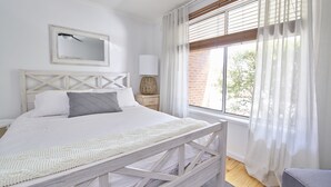 Et soveværelse med seng, natbord, lampe, spejl og et vindue med gardiner.