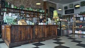 Un café avec un comptoir en bois, des étagères remplies d’ustensiles de cuisine, une machine à café et une vitrine où sont exposées des pâtisseries.