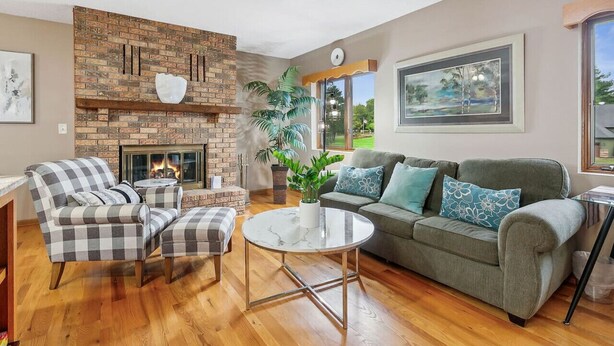 A living room with a brick fireplace, a sofa, a chair, a round table, and a large window.
