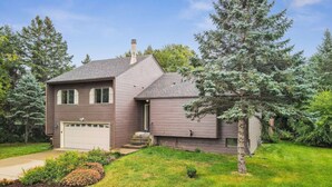 A two-story house with a garage, a front yard with a lawn and a flower bed, and a large evergreen tree.