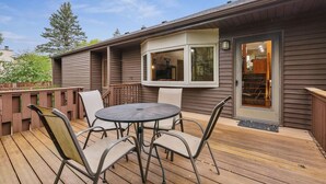 A deck with a table and chairs, a window, and a door leading to a covered area.