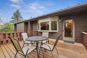 A deck with a table and chairs, a window, and a door leading to a covered area.