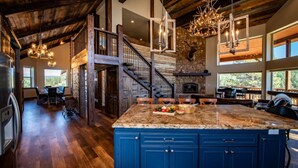 A spacious kitchen with a large island, wooden flooring, and a stone fireplace. - Luxury Retreat w/ Hot Tub, Sauna, Firepit, 360 Views, 140 Acres (Pagosa Springs)