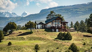 A large, multi-story lodge with a prominent tower, situated on a grassy hill with a mountainous backdrop. - Luxury Retreat w/ Hot Tub, Sauna, Firepit, 360 Views, 140 Acres (Pagosa Springs)