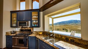 A kitchen with dark cabinets, stainless steel appliances, a granite countertop, and a window offering a view of a hilly landscape. - Luxury Retreat w/ Hot Tub, Sauna, Firepit, 360 Views, 140 Acres (Pagosa Springs)