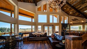 A spacious living area with a large leather sofa, a wooden bar, and a view of the outdoors. - Luxury Retreat w/ Hot Tub, Sauna, Firepit, 360 Views, 140 Acres (Pagosa Springs)