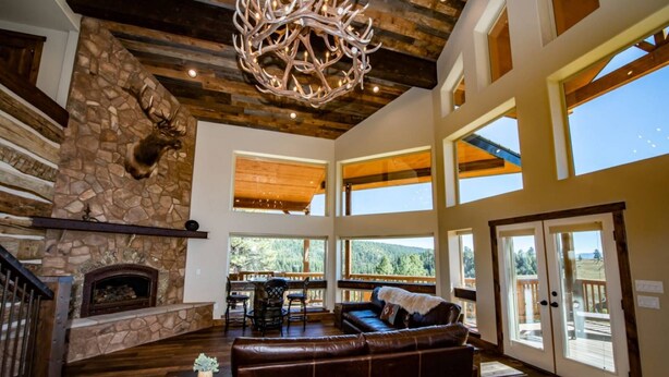 A spacious living area with a stone fireplace, leather sofa, and large windows offering views of the outdoors. - Luxury Retreat w/ Hot Tub, Sauna, Firepit, 360 Views, 140 Acres (Pagosa Springs)
