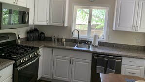 A kitchen with white cabinets, a stainless steel stove, a microwave, a sink, and a window with a view of greenery. - Pleasant Street Suite in downtown Prescott (Prescott)