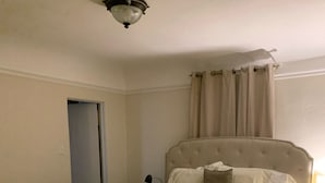 A neatly made bed in a room with a door, a small table with a lamp, and a ceiling light fixture. - Pleasant Street Suite in downtown Prescott (Prescott)