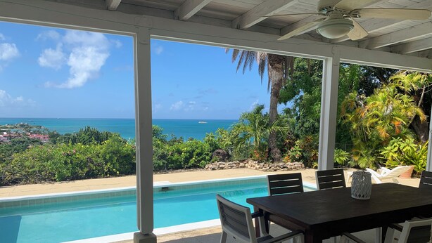 Un espace extérieur abrité comprenant une piscine, des chaises blanches et une table.