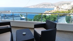 A balcony with wicker furniture, a view of the sea, and buildings in the background. - Hotel Bella Vista (Sarandë)