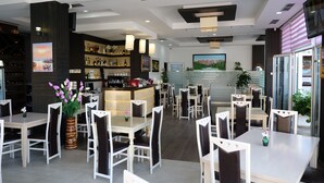 A modern restaurant with multiple dining tables and chairs, a bar area with shelves of bottles, and a large painting on the wall. - Hotel Bella Vista (Sarandë)