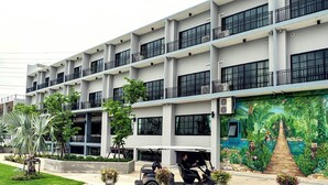 A multi-story hotel with balconies, a mural of a jungle scene, and a parking area with a scooter.