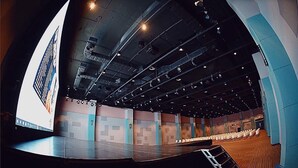 A large, modern auditorium with tiered seating, a stage, and a large screen displaying a logo.
