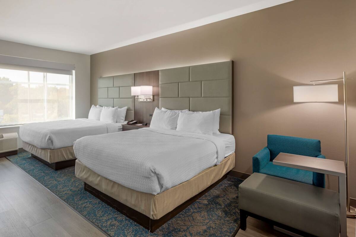A hotel room with two beds, a sofa, a desk, and a lamp.