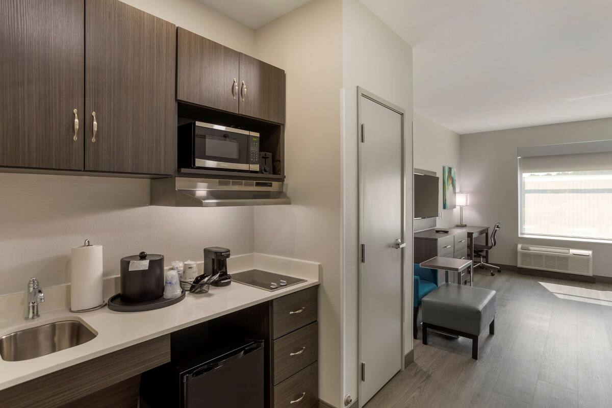 A modern kitchen with a microwave, coffee maker, and a sink. There is a dining area with a table and chairs.