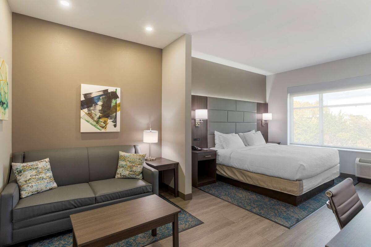 A modern hotel room with a sofa, a bed, a nightstand, and a window with a view.