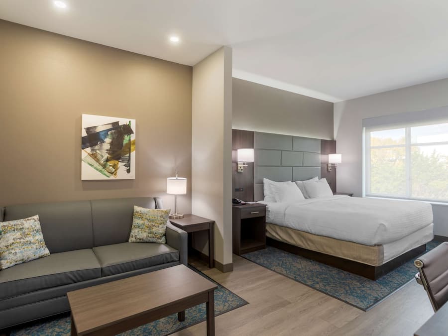 A modern hotel room with a sofa, a bed, a nightstand, and a window with a view.
