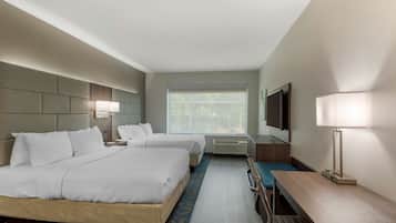 A hotel room with two beds, a desk, a chair, a TV, and a window with a view of trees.