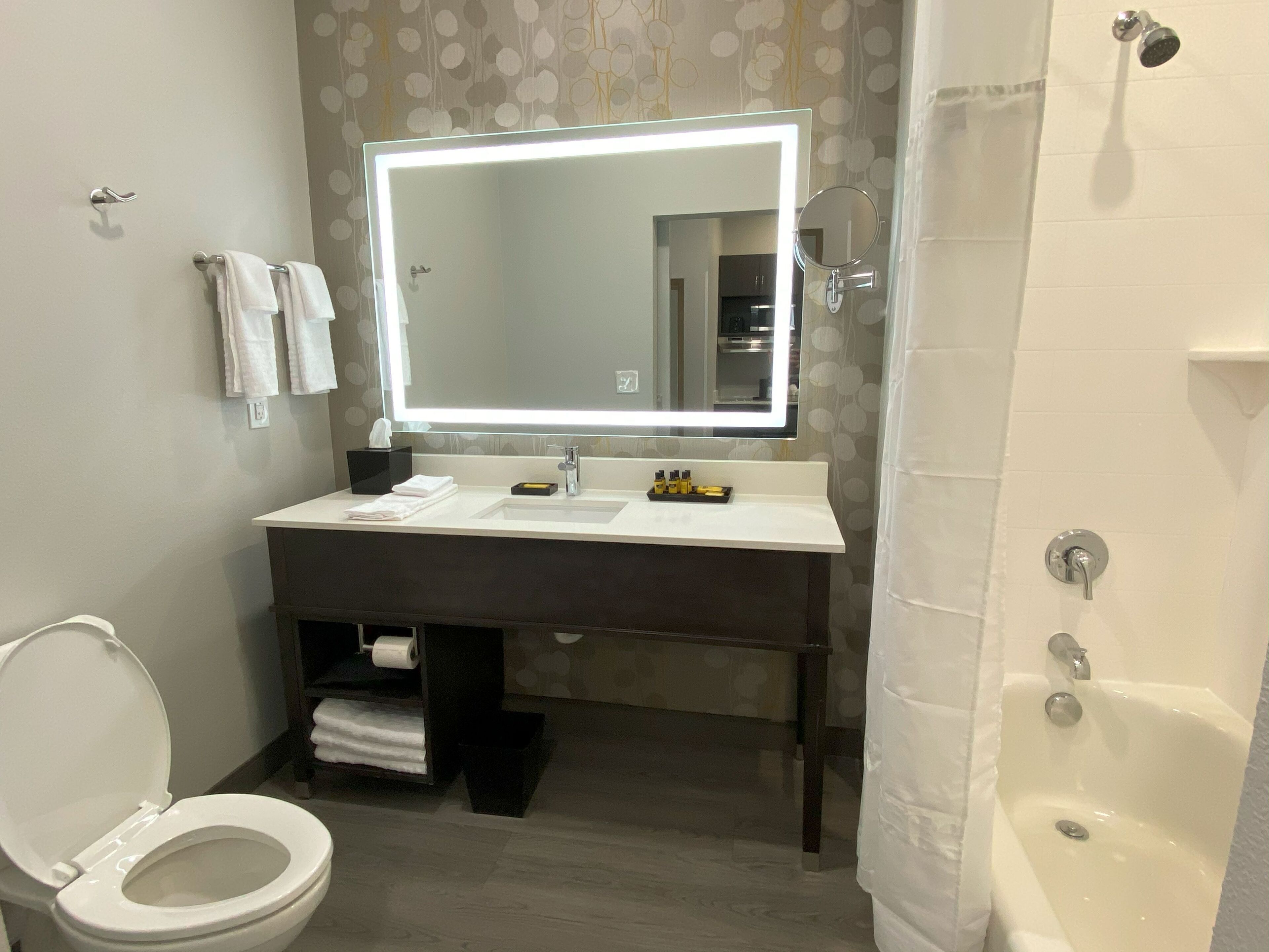 A modern bathroom with a white sink, a large mirror with integrated lighting, a toilet, and a bathtub.
