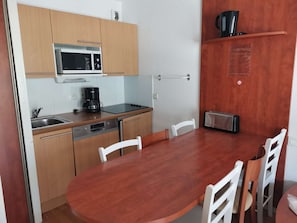 Cozinha compacta com micro-ondas, cafeteira, torradeira e pia. Mesa de jantar de madeira com cadeiras.
