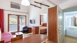 A room with a wooden table, chairs, a TV, a bed, and a balcony with a view. - Pleasant duplex with parking - 7 guests (La Mongie)
