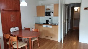 A compact kitchen with a microwave, coffee maker, and a toaster on the counter. There is a wooden dining table with chairs. - Charming studio - 4 guests - Near slopes (La Mongie)