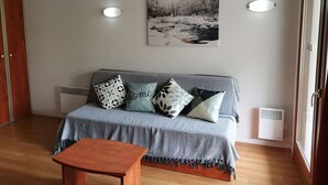 A cozy living room with a grey sofa, patterned cushions, a small wooden table, and a framed picture on the wall. - Charming studio - 4 guests - Near slopes (La Mongie)