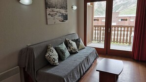 A cozy room with a sofa, a small table, and a painting on the wall. - Charming studio - 4 guests - Near slopes (La Mongie)