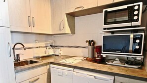 Une cuisine compacte avec des meubles blancs, un lave-vaisselle, un four à micro-ondes et une machine à café.