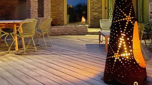 A wooden deck with a stone fireplace, outdoor seating, and a decorative light sculpture. - Mushroom House, Earl Young’s Personal Residence overlooking Lake MI! New AC!  (Charlevoix)