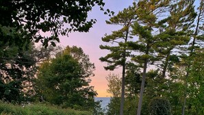 A grassy park area with a stone pathway, surrounded by trees and a view of the water. - Mushroom House, Earl Young’s Personal Residence overlooking Lake MI! New AC!  (Charlevoix)