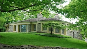 A stone house with a curved roof, large windows, and a well-maintained lawn. - Mushroom House, Earl Young’s Personal Residence overlooking Lake MI! New AC!  (Charlevoix)
