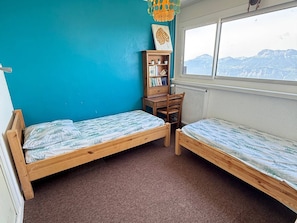 Een kamer met twee houten bedden, een bureau, een boekenkast en een raam met uitzicht op de bergen.