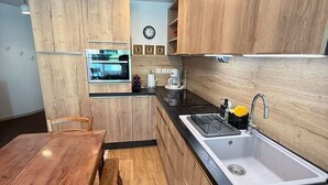 A modern kitchen with wooden cabinets, a built-in oven, a sink, and a dining area with a bench. - 3-room apartment at the foot of the slopes, 7th floor (Les Adrets-Prapoutel)