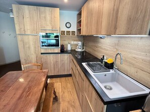 Een moderne keuken met houten kastjes, een inbouwoven, een spoelbak en een eethoek met een bank.