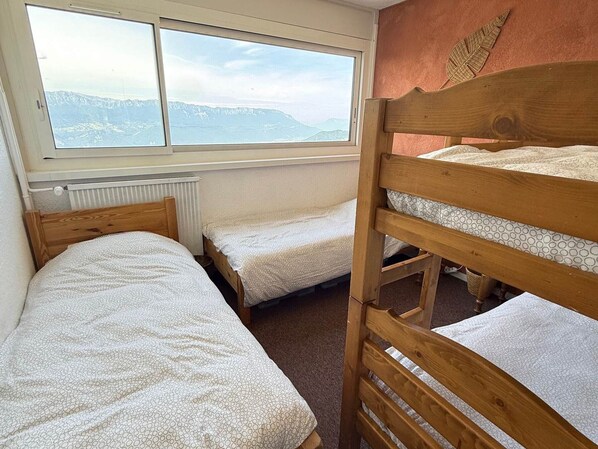 A dormitory room with bunk beds, a radiator, and a window with a mountain view.