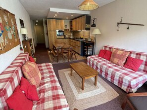 A living room with a sofa set, a wooden coffee table, and a kitchen area with wooden cabinets and a dining table.