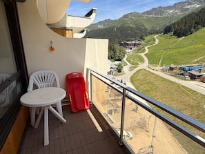 Een balkon met een tafel en stoelen, met uitzicht op een bergachtig landschap met een skilift en gebouwen.