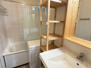 Een badkamer met een wit wastafelmeubel, een spiegel en een houten plank.